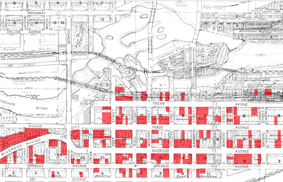 A detailed street map showing a grid layout with highlighted sections in red. Key street names include Riverside Avenue, Sprague Avenue, Main Avenue, and Trent Avenue. The Spokane River is marked, and several train yards and railway lines are shown. The map contains various numbered plots, with some areas shaded in red, likely indicating significant areas or properties.