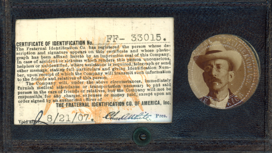 A certificate of identification labeled "FR-33015" from The Fraternal Identification Co. of America, Inc. Text describes procedures in case of accident or sickness, indicating that information will be sent to relatives. It states the company will provide assistance but not cover expenses without an authorized order. The document is signed by "Chas H. White" as President and is marked void after "8/21/07." Next to the text is a circular image showing a man wearing a hat and glasses.