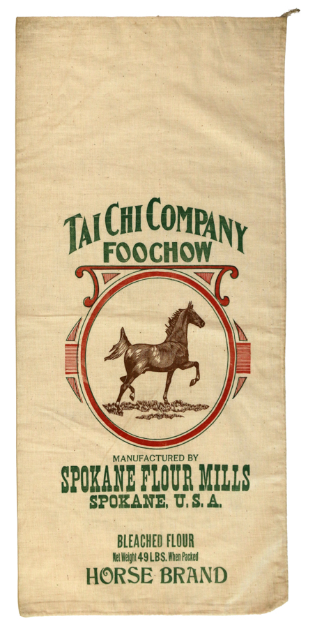 A fabric sack with the text "Tai Chi Company Foochow" and an image of a horse inside a circular frame. Below the horse, it reads "Manufactured by Spokane Flour Mills Spokane, U.S.A." The text at the bottom says "Bleached Flour Net Weight 49 Lbs. When Packed Horse Brand."