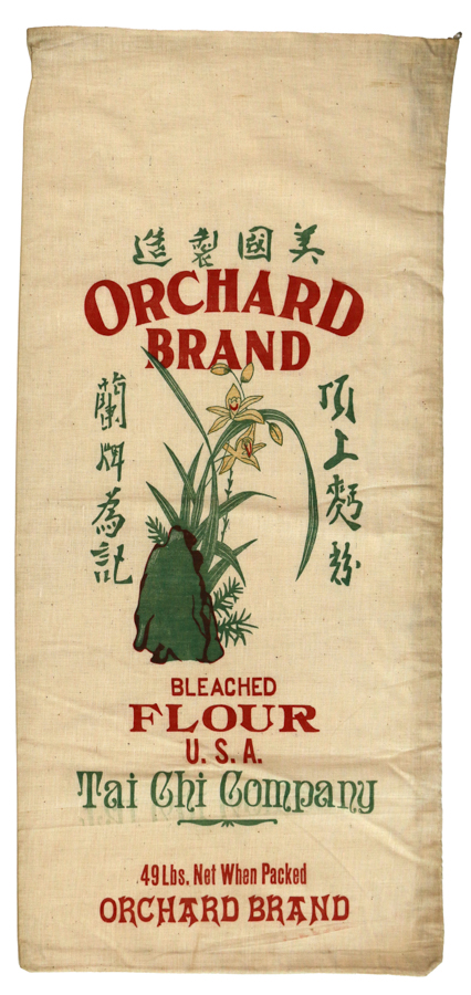 A fabric sack with text and illustrations. The text reads "Orchard Brand" prominently at the top, followed by "Bleached Flour U.S.A.," and "Tai Chi Company." At the bottom, it states "49 Lbs. Net When Packed Orchard Brand." There are Chinese characters on it as well. The illustration features flowers and leaves near a rock.