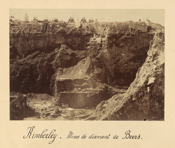 A large open-pit mining site with steep rock walls and various mining structures on the edge. Equipment and cables are visible on the site. The text at the bottom reads: 