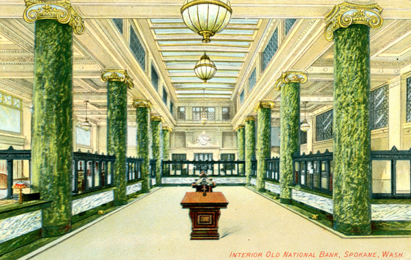 An ornate interior with tall green marble columns, decorative ceiling details, and multiple hanging light fixtures. There is a central wooden table in the middle of the space. The surrounding area has teller windows with dark frames. The text reads: 