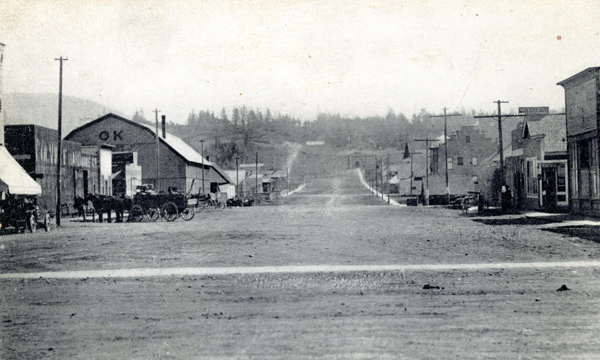 A wide street lined with wooden buildings stretches into the distance. On the left, a building with 