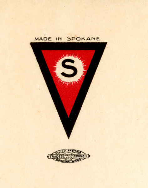 A triangular emblem with a red interior and a black border, containing a large letter 