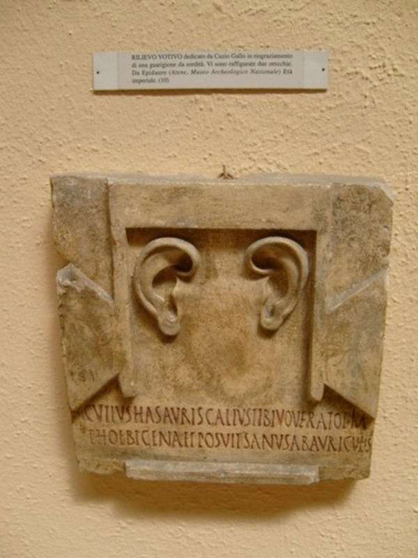 A first centry carved marble tablet from depicting two ears in the center and a Latin inscription below translating roughly to “Cutius Gallus once vowed these ears to you, offspring of Phoebus, now] being healthy as regards [his] ears.”