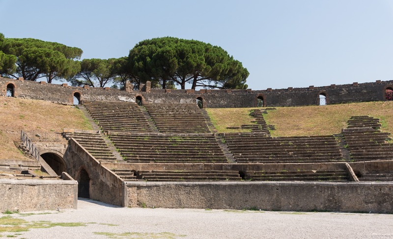 Interior view of the ancient stone amphitheater at Pompeii with seating around the arena floor.