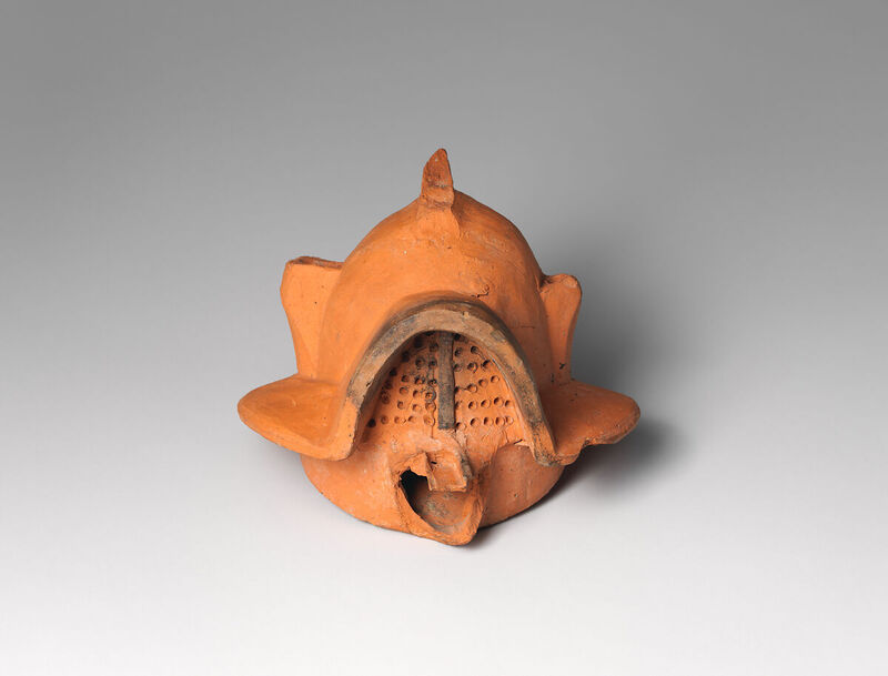 Terracotta oil lamp shaped like a Roman gladiator helmet with a central crest and face guard.